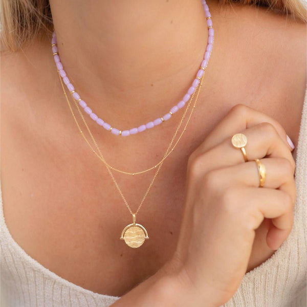 Damen mit zwei Gold Halskette mit elegantem Anhänger mit Wellenmuster und einer Perlenhalskette in lila. | STYLE: Aloita